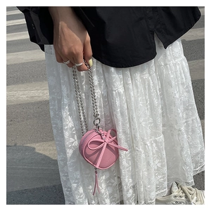 Detalle del mini bolso bandolera rosa con forma de corazón, lazo 3D y cadena de bolas