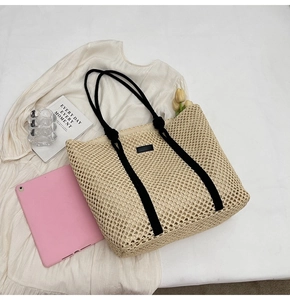 Detail of hand-woven straw tote bag with black rope handles and minimalist leather tag