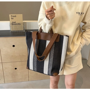 Detailed view of large canvas tote bag featuring vertical stripes and brown leather corners