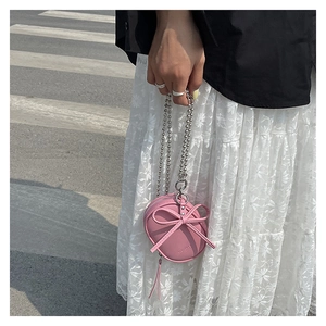 Detalle de un mini bolso bandolera rosa con un lazo y cadena de bolas plateadas
