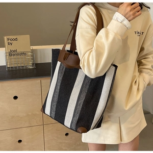 Model wearing a large striped canvas tote bag with brown leather handles and base