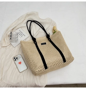 Flat lay of a beige woven tote bag with black rope handles on a cream dress background