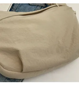 Détail du sac à bandoulière en nylon beige avec fermeture éclair et design incurvé