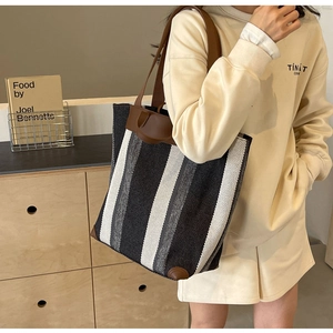 Close-up of a large striped canvas tote bag with brown leather trim and shoulder straps