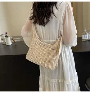 Detail of a beige hollow knit tote bag styled with a white pleated dress in a cafe