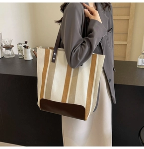 Vertical canvas tote with contrasting stripes and brown leather handles on a female model