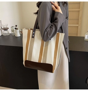Detail of striped canvas tote bag with brown leather base on model's shoulder in office