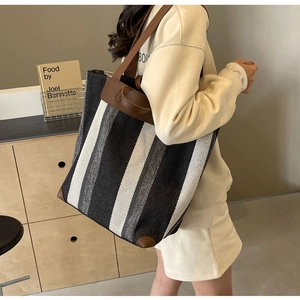 Close-up of a striped canvas tote bag with leather trim worn on the shoulder of a model