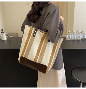 Detail of striped canvas tote bag showing dark brown shoulder strap and metal rivets