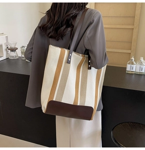 Close-up of striped canvas tote bag detail featuring brown leather base and metal rivets