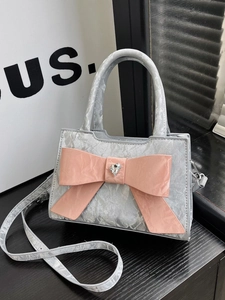 Silver shoulder bag featuring a large pink bow and heart rhinestone on a wooden table