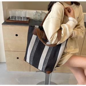 Detail view of large striped canvas tote bag with brown leather straps and reinforced corners