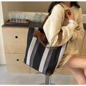 Detail of a large striped canvas tote bag with brown leather reinforcement on the shoulder