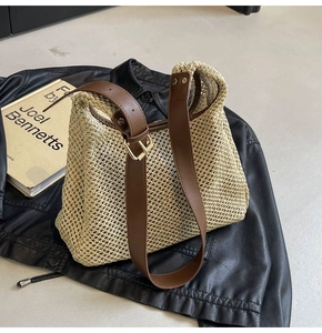 Detail of woven straw shoulder bag featuring brown leather strap and gold buckle