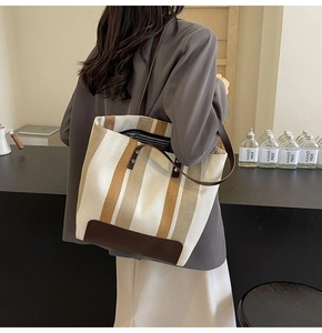 Detail of striped canvas tote bag showing dark brown leather handles and base contrast