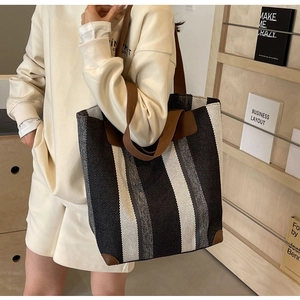 Detail of striped canvas tote bag showing reinforced brown leather corners and texture