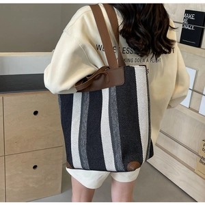 Detail of striped canvas tote bag with brown handles and reinforced leather corners