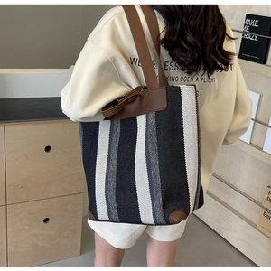 Detail of striped canvas tote bag with brown leather reinforcement and wide straps