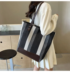 Detail of striped canvas tote bag with brown leather straps shown on shoulder