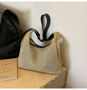 Detail of beige woven tote bag with black leather strap on a natural stone surface