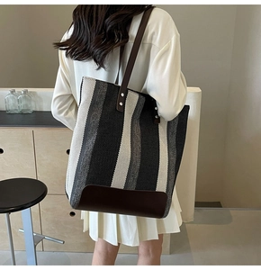 Detail of large striped canvas tote bag with brown leather handles and metal rivets