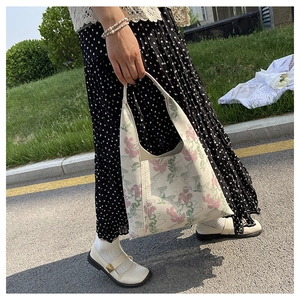 Detail of floral embroidery on a vintage beige canvas hobo bucket bag in outdoor setting