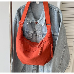 Détail du sac croissant en nylon orange avec large bandoulière et tirette tressée sur jean