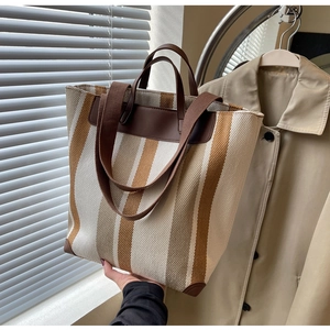 Detail of canvas tote bag with brown stripes, leather trim, and dual shoulder straps