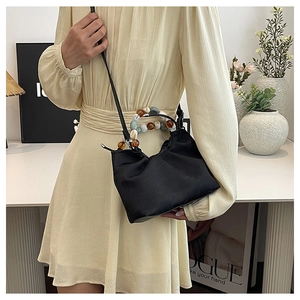 Détail d'un sac à main noir en tissu avec poignée en perles de résine et bandoulière longue