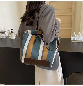 Detail of a large striped canvas tote bag with brown leather straps shown on a model