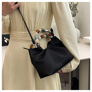 Détail du sac à main plissé noir avec poignée en perles et texture satinée élégante