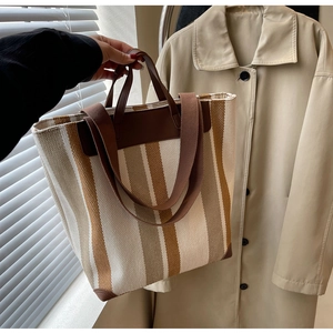 Detailed view of canvas tote bag with brown stripes and leather trim reinforcement