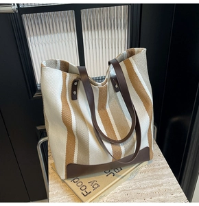 Detail of striped canvas tote bag with brown leather handles and metal rivet reinforcement