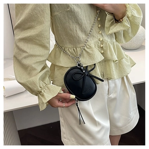 Detalle de un mini bolso negro con lazo 3D y cadena de bolas plateadas en un modelo