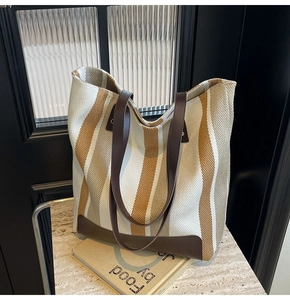 Detail of vintage striped canvas tote bag with brown leather handles on stone surface