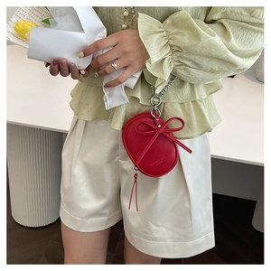 Primer plano de un pequeño bolso redondo rojo de cuero con lazo y cadena de plata en modelo