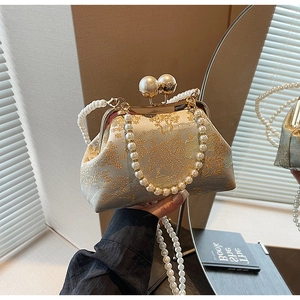 Detailed view of retro embroidery handbag featuring gold floral pattern and large pearl clasp