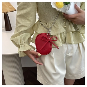 Detalle de un mini bolso bandolera redondo rojo con lazo y cadena de bolas plateada