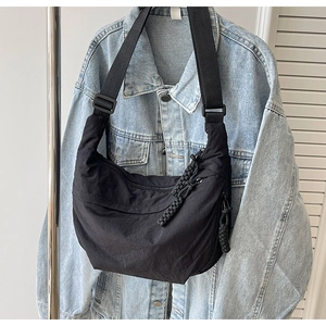 Détail d'un sac demi-lune en nylon noir avec bandoulière réglable et tirette en corde tissée