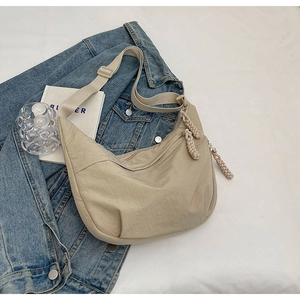 Détail du sac bandoulière beige en nylon avec tirette tissée sur une veste en jean