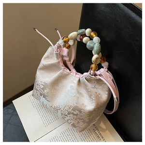 Détail d'un sac seau en jacquard rose avec poignée en perles colorées sur un siège en cuir