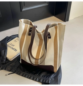 Detail of striped canvas tote bag with brown leather handles and reinforced metal rivets