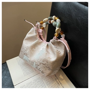 Détail du sac en brocart rose avec motif paysage et anse en grosses perles colorées