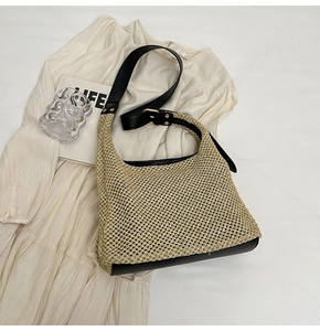 Detail of beige woven straw tote with black leather straps and metal buckles on fabric