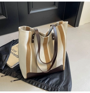 Detailed view of striped canvas tote bag with leather handles on leather background