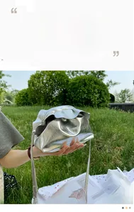 Close-up of metallic silver drawstring cloud bag with pleated ruffle details on grass