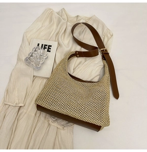 Detail of woven straw tote with brown leather base and adjustable strap on a lifestyle background