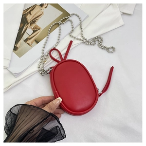 Detalle de mini bolso ovalado rojo con cadena de bolas plateada sobre tela blanca