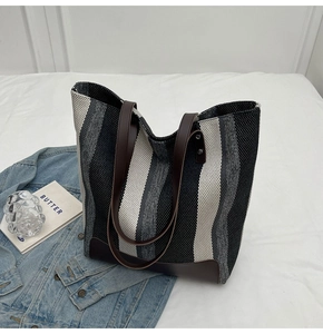 Detail of striped canvas tote bag with brown leather handles on a minimal white background