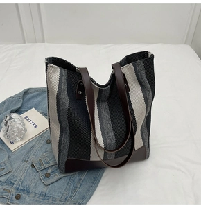 Detailed view of striped canvas tote bag with brown leather handles and reinforced base corners